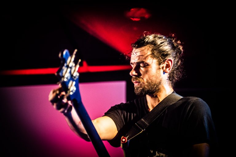 Een muzikant speelt een elektrische basgitaar op een podium met kleurrijke verlichting.