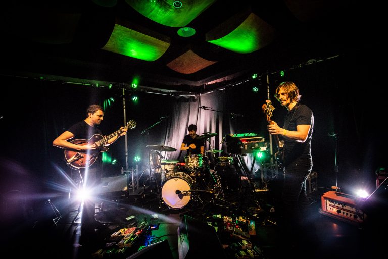 Een band speelt live op het podium met groene verlichting en verschillende instrumenten.