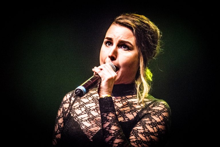 Zangeres met een microfoon, gekleed in een zwarte kanttop, tijdens een optreden.