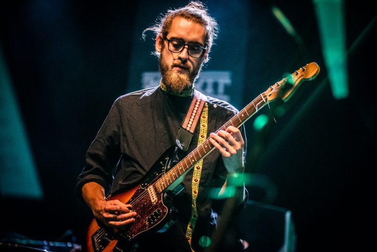 Een muzikant speelt gitaar op een podium met sfeervolle verlichting.