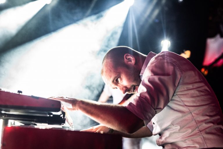 Een muzikant speelt intens op een keyboard, omgeven door heldere lichten en rook.