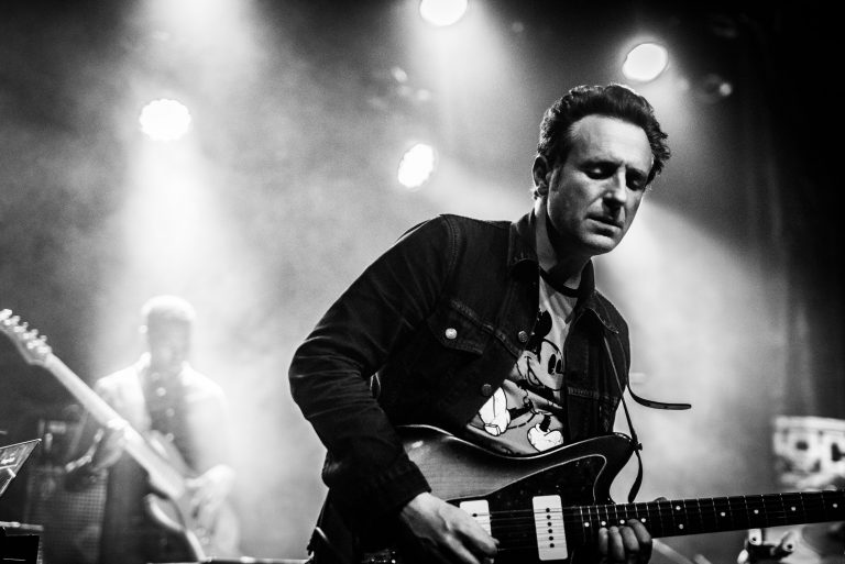 Een muzikant speelt gitaar op een podium met sfeerverlichting.