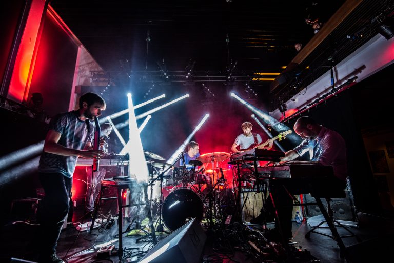Een band speelt live muziek op het podium met kleurrijke lichtstralen.