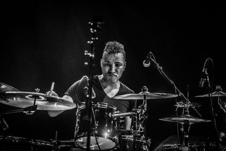 Een drummer speelt op een drumstel tegen een donkere achtergrond.