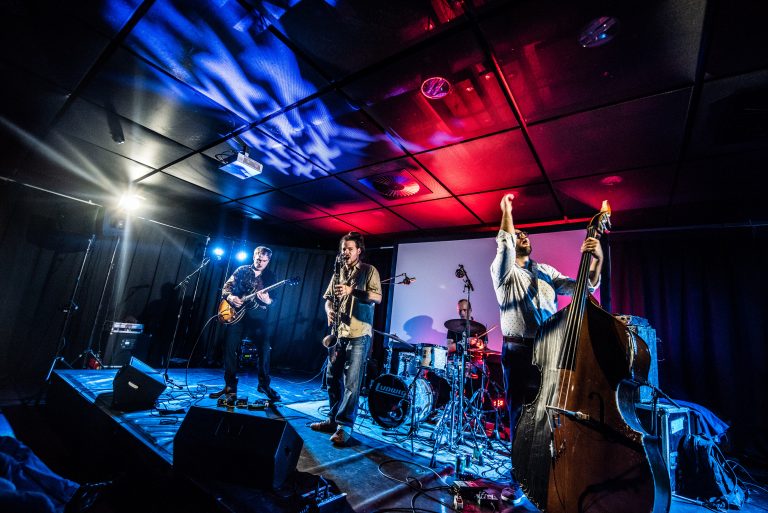 Een live band treedt op met verschillende muzikanten op het podium, verlicht door kleurrijke lichten.