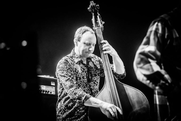 Een muzikant speelt een contrabas op een podium, gefotografeerd in zwart-wit.