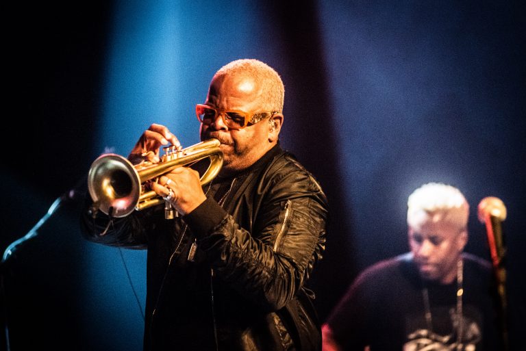 Een muzikant speelt trumpet op een podium, met een focus op zijn expressieve voorkomen in een sfeervolle belichting.