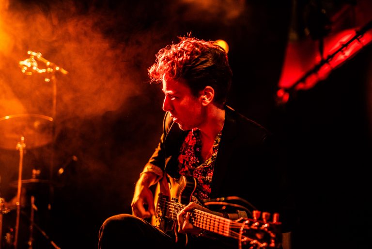 Een muzikant speelt op een elektrische gitaar in een sfeervolle, lichtgevende omgeving.