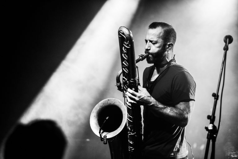 Een muzikant speelt een groot blaasinstrument op een podium, omgeven door sfeerverlichting.