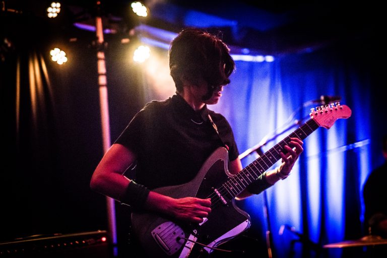 Een muzikant speelt gitaar op een podium met sfeervolle verlichting.