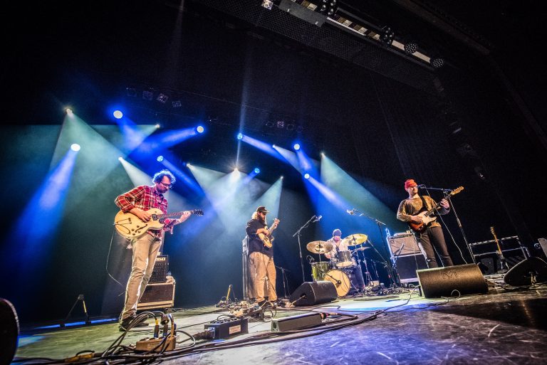 Een live band performt op een podium met kleurrijke lichtstralen.