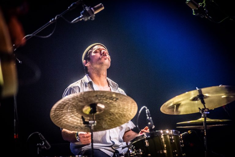 Een drummer in een lichteffect-rijke omgeving, geconcentreerd op het spelen van zijn instrument.