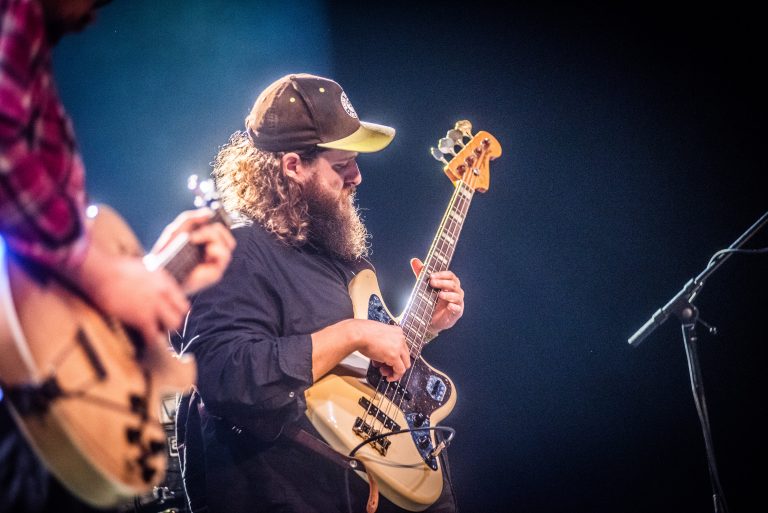 Een muzikant met een hoed speelt een elektrische gitaar op het podium tijdens een optreden.