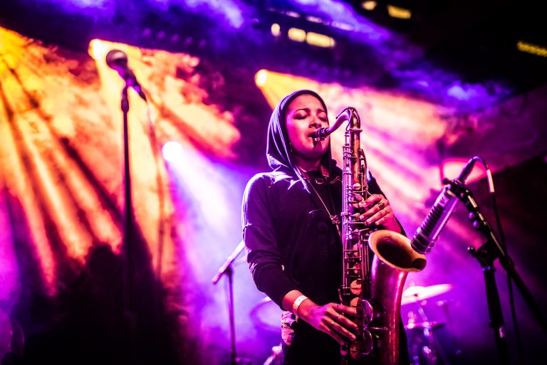 Een muzikant speelt saxofon op een podium met kleurrijke verlichting.