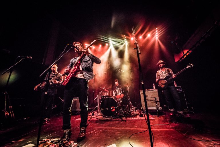 Een band speelt live muziek op een podium, verlicht door kleurrijke lichteffecten.