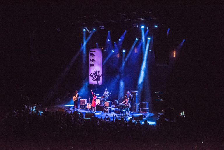 Een band speelt live op een podium met kleurrijke lichten en een enthousiast publiek.