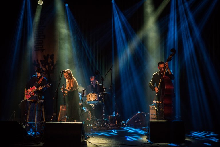 Een band staat op een podium met kleurrijke verlichting terwijl ze muziek spelen.