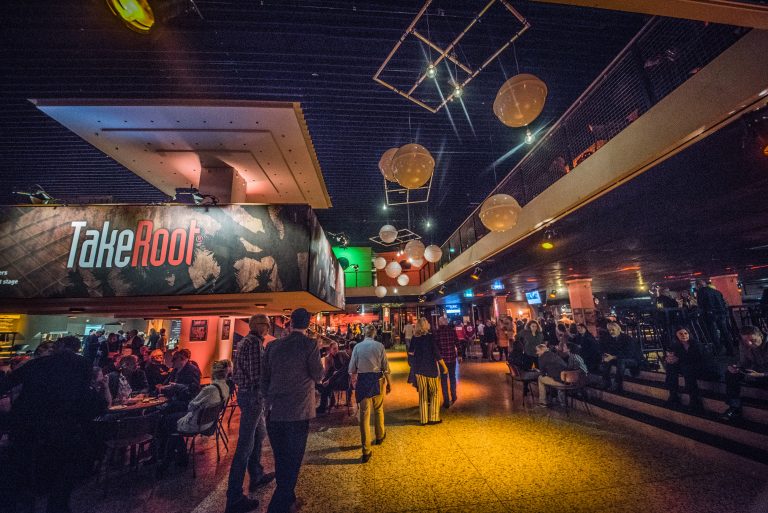 Drukke inrichting van een gezellige bar met dimlicht, bezoekers en opvallende verlichtingselementen.