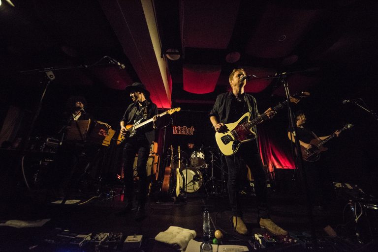 Een band speelt live muziek op een podium met gedimd licht en een intieme sfeer.