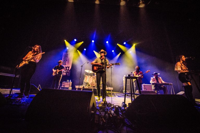 Een band speelt live op een podium met gekleurde verlichting.