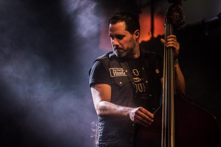 Een muzikant speelt contrabas op een podium, omgeven door sfeervolle rook en verlichting.
