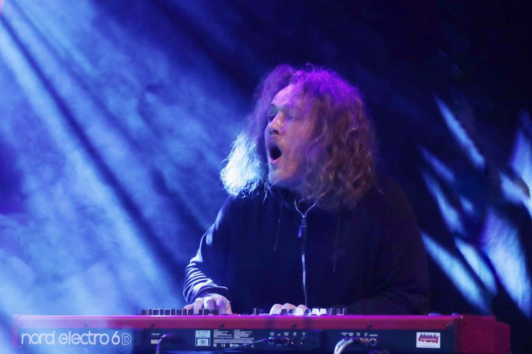 Een muzikant speelt enthousiast op een keyboard onder kleurrijke lichteffecten.