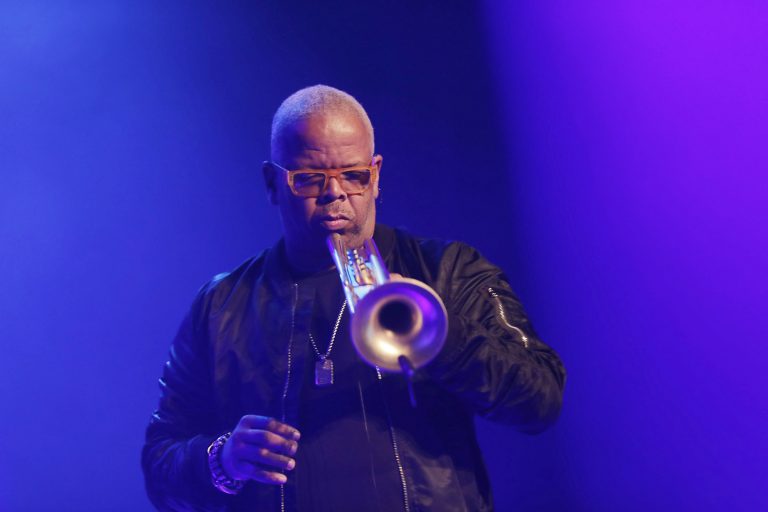 Een muzikant speelt op een trompet onder kleurrijke verlichting.