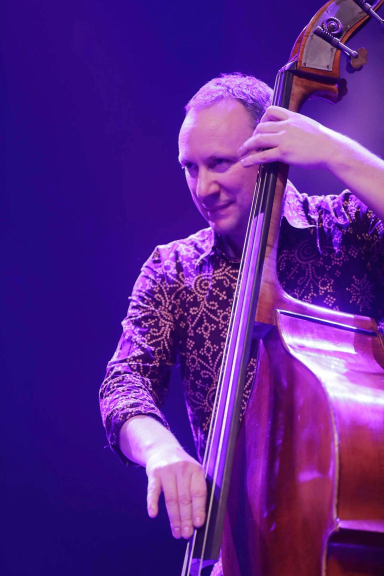 Een muzikant speelt op een contrabas, omgeven door paarse verlichting.