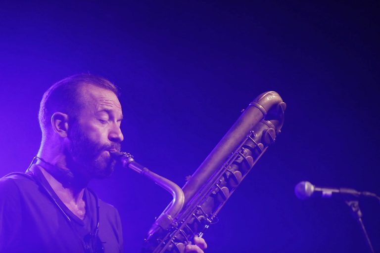 Een muzikant speelt op een baritonsaxofoon onder een blauwe verlichting.