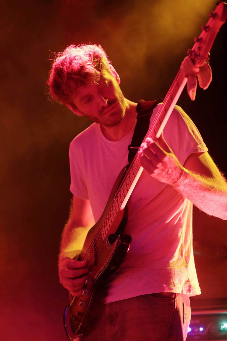 Een muzikant speelt basgitaar op een podium, omgeven door kleurrijke verlichting.