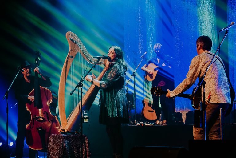 Een muzikale uitvoering met een harpspeler en andere muzikanten op een verlicht podium.