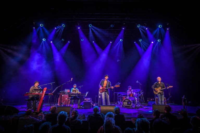 Een liveband speelt op een podium met paarse verlichting.