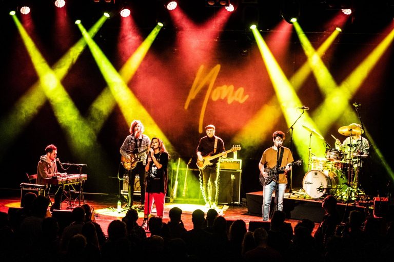 Een band voert live muziek op met kleurrijke verlichting op het podium, terwijl een menigte naar het optreden kijkt.