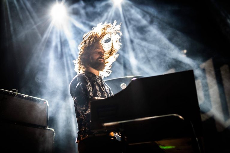 Een muzikant speelt piano onder opvallende lichtstralen, met zijn haar in beweging.