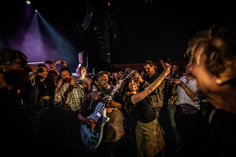 Een drukke concertcrowd met mensen die genieten van de muziek en selfies maken.