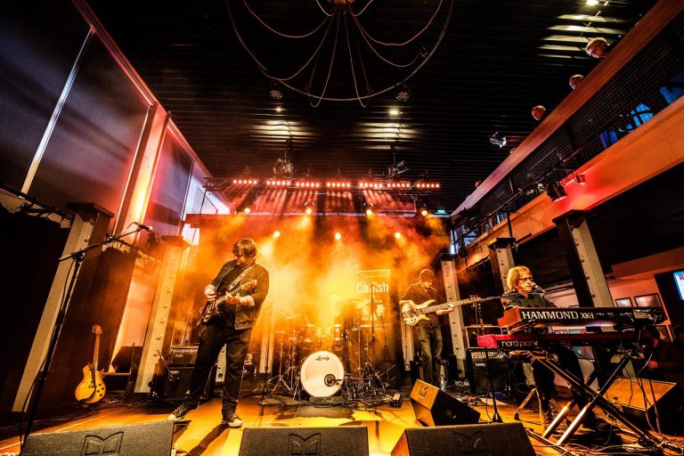 Een band speelt live op een podium met kleurrijke verlichting en rookeffecten.