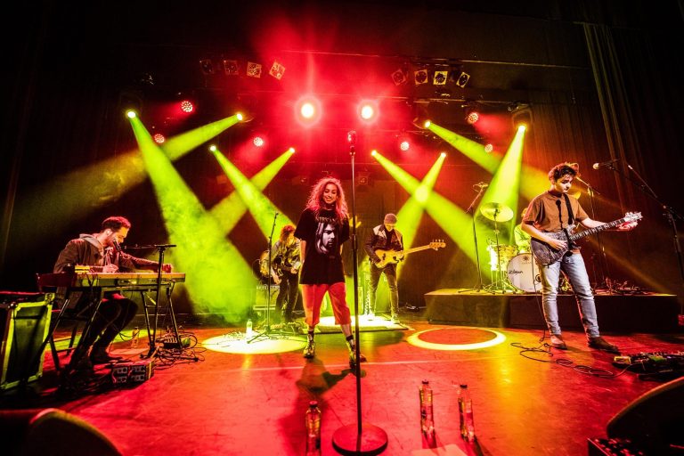 Een muzikale uitvoer met een band die optreedt op een verlicht podium met kleurrijke lichten.