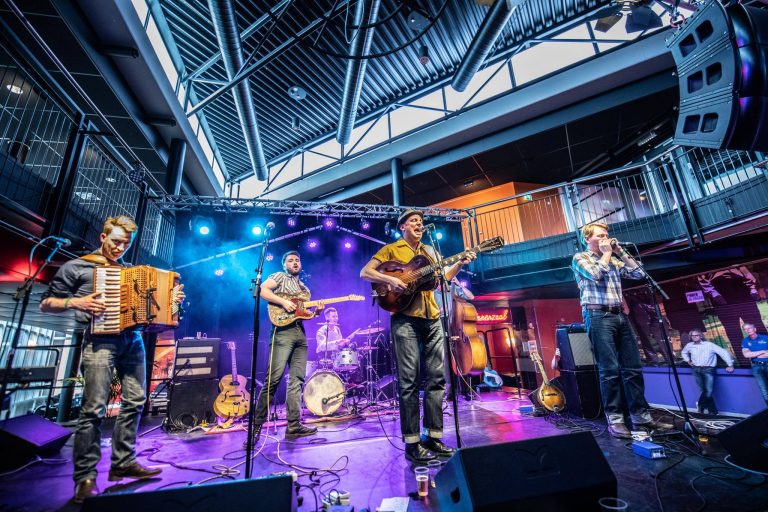 Een band speelt live muziek op een podium met kleurrijke verlichting in een grote ruimte.