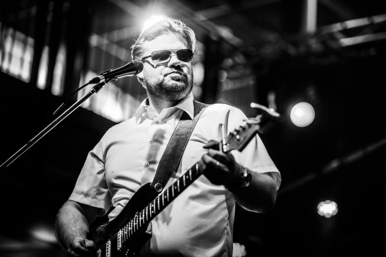 Een muzikant speelt gitaar op een podium met felle verlichting.