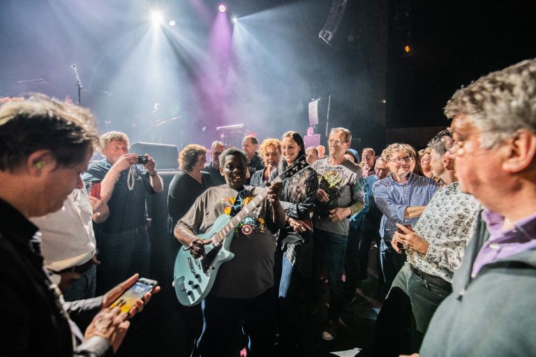 Een feestelijke menigte geniet van een live optreden met een muzikant die een elektrische gitaar speelt.