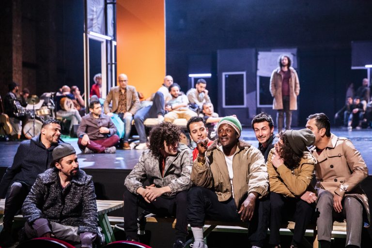 Een groep mensen zit op het podium van een theater in een moderne, artistieke setting.