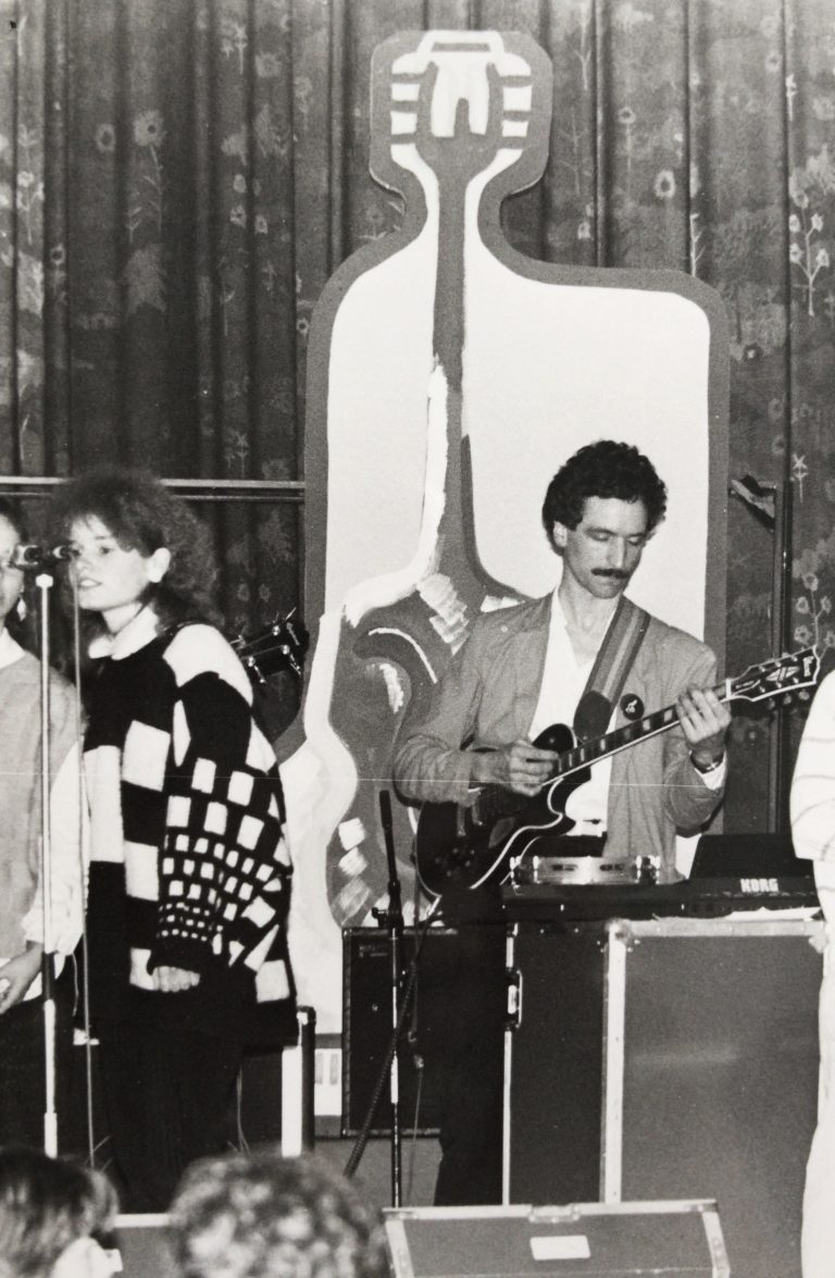 Een zwart-wit afbeelding van een band die live optreedt, met zangers en een gitarist.