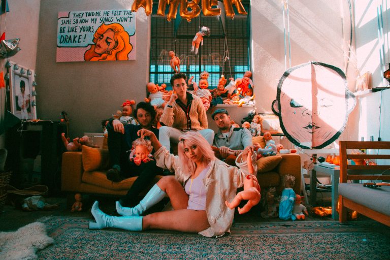 Groep mensen zit op een bank in een gekleurde kamer vol met speelgoed en decoraties.