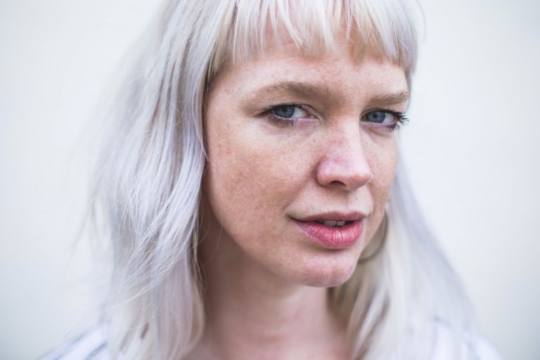 Portret van een vrouw met lang, lichtblond haar en een serieuze uitstraling.