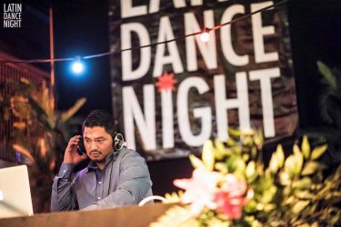 Een DJ draait muziek achter een mixer met een 'Dance Night'-decor op de achtergrond.