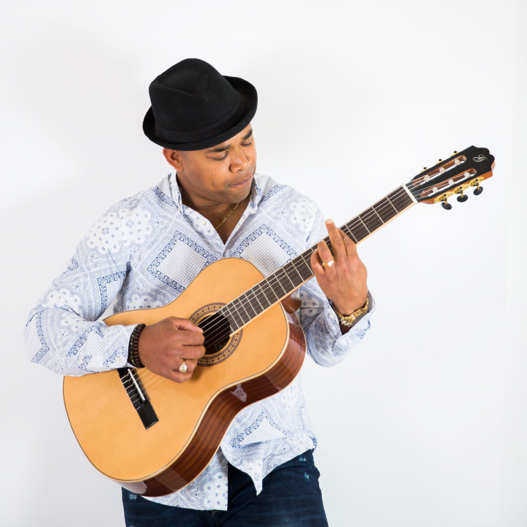 Een man in een hoed speelt gitaar tegen een witte achtergrond.