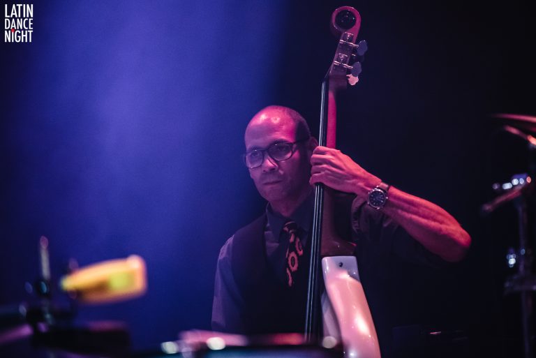 Een muzikant speelt contrabas op een podium met zachte, gekleurde verlichting.
