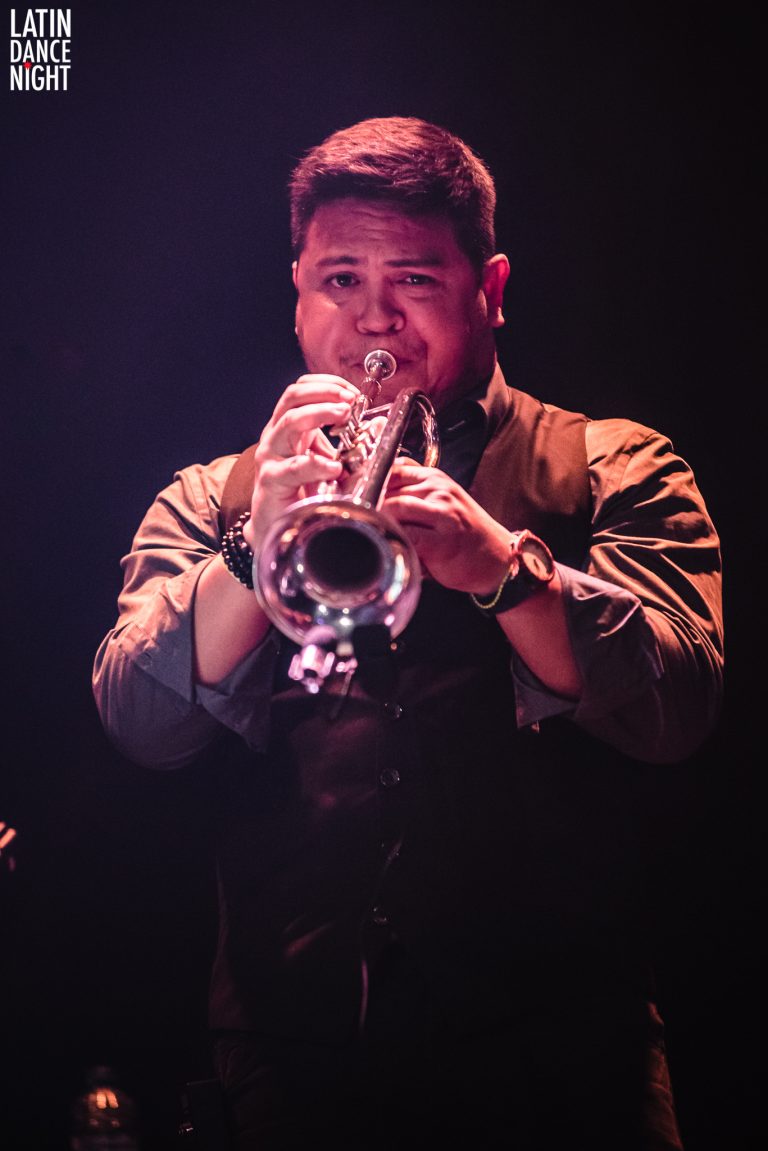 Een muzikant speelt op een trompet onder sfeervolle verlichting.