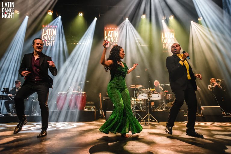 Een energiek muziekoptreden met drie artiesten die dansen op een verlichte podium.