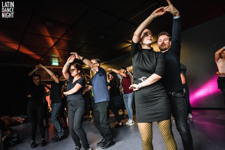 Groep mensen danst samen in een leuke setting met raised handen en energieke houdingen.